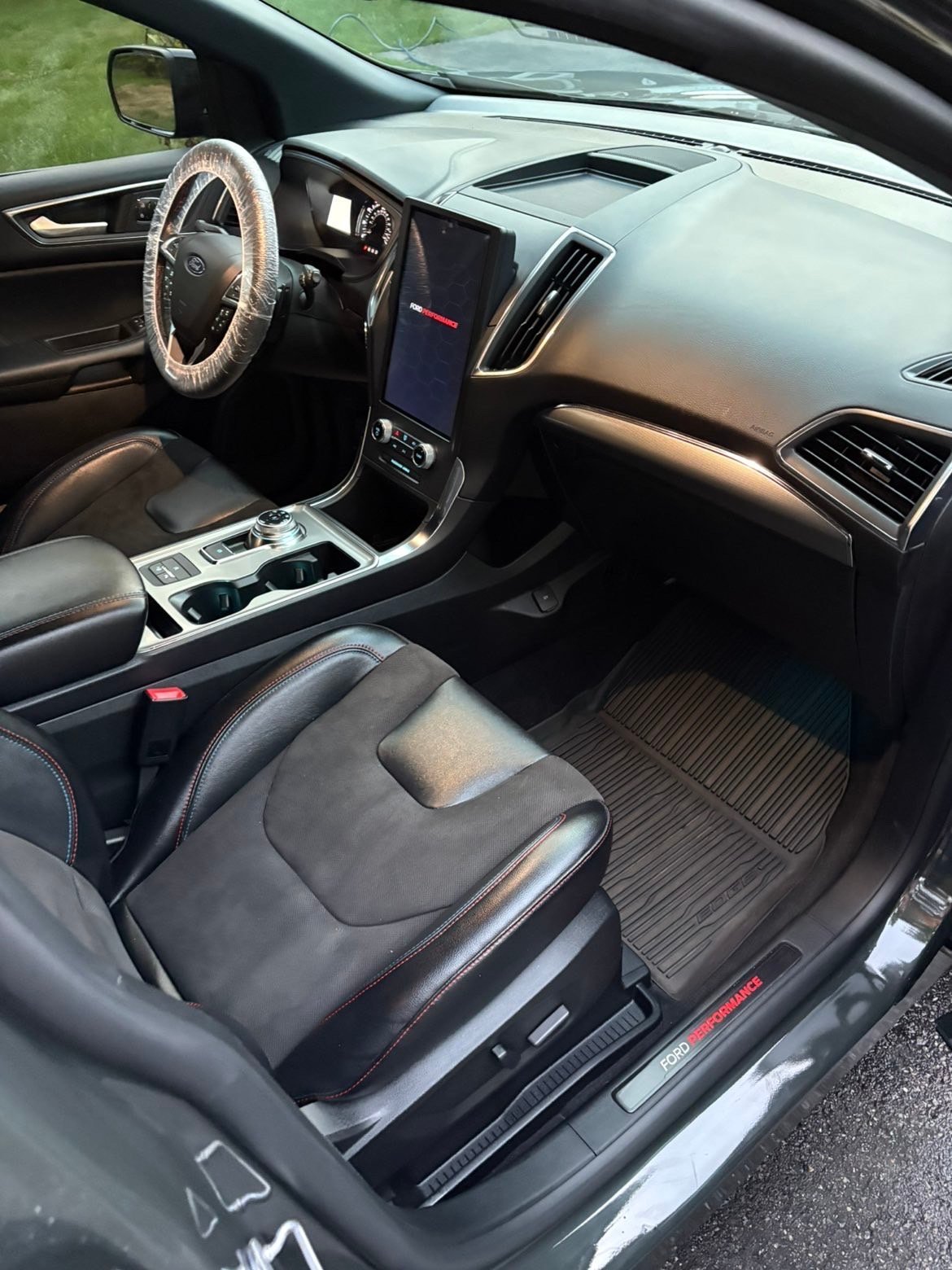 Interior of a modern vehicle showing leather seats, steering wheel, central touchscreen, and dashboard with the door open